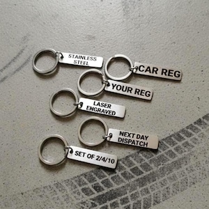 May include: Several stainless steel keyrings with rectangular tags. The tags are engraved with various phrases: "STAINLESS STEEL", "CAR REG", "YOUR REG", "LASER ENGRAVED", "NEXT DAY DISPATCH", and "SET OF 2/4/10".