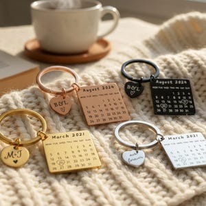 Puede incluir: Varios llaveros personalizados con dijes de calendario y forma de corazón. Los llaveros son de color oro, plata, negro y oro rosa. Algunos dijes tienen iniciales y fechas, como "Marzo 2021" y "Agosto 2024".