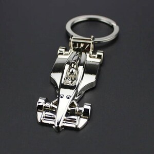 May include: A silver metal keychain featuring a detailed model of a race car. The car has a driver in the cockpit and is attached to a silver key ring.