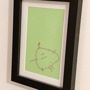 May include: A framed drawing of a simple cartoon character with a red marker on a green background.