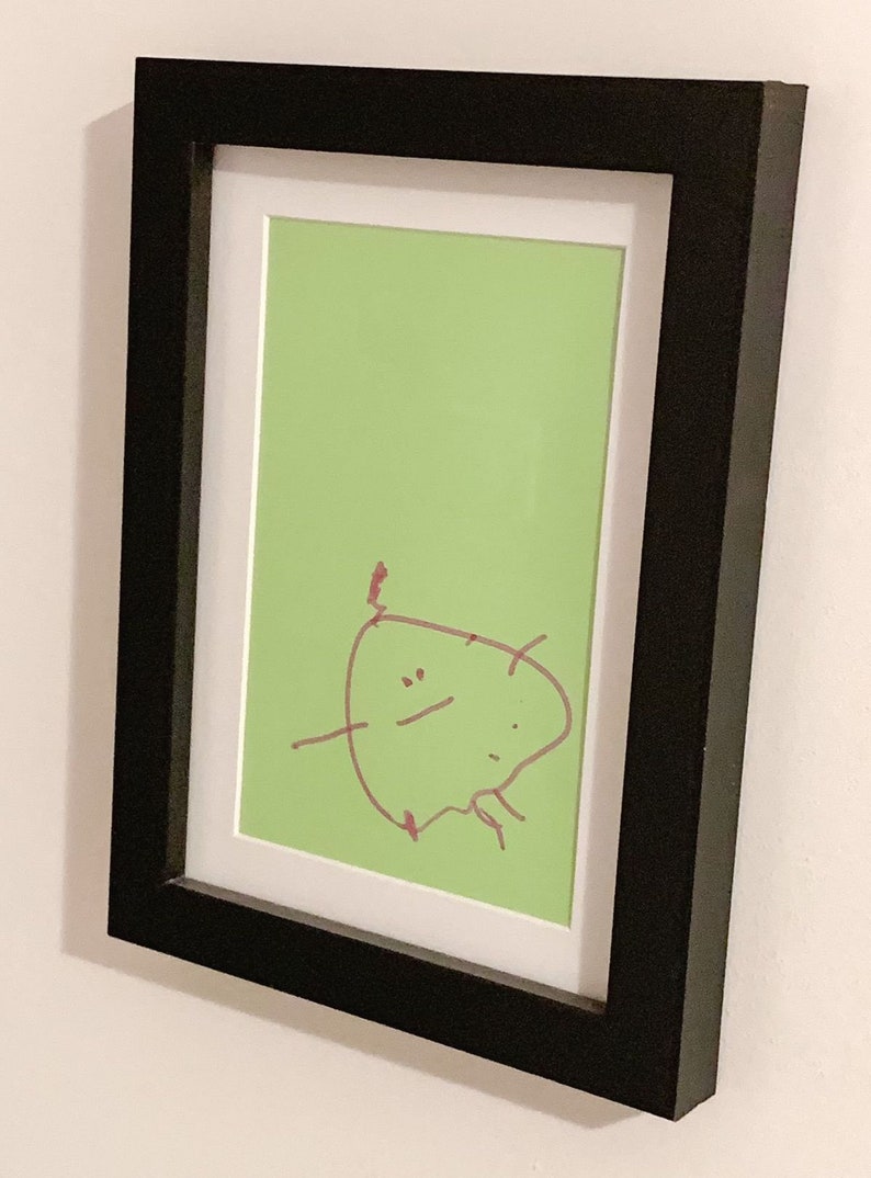 May include: A framed drawing of a simple cartoon character with a red marker on a green background.