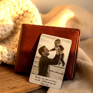 Puede incluir: Una cartera de cuero marrón con una tarjeta personalizada con una foto en blanco y negro de un padre y un niño. La tarjeta tiene el texto "Daddy, now you can carry me too. Wherever you go. Ryan xxx."