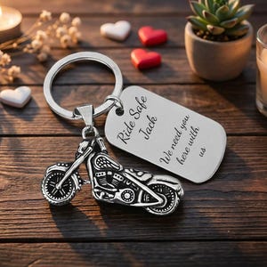 May include: A silver motorcycle keychain with a matching tag. The tag reads "Ride Safe Jack, We need you here with us." The keychain is on a wooden surface with candles, hearts, and a small plant.