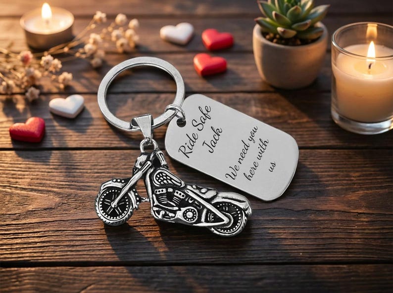 May include: A silver motorcycle keychain with a matching tag. The tag reads "Ride Safe Jack, We need you here with us." The keychain is on a wooden surface with candles, hearts, and a small plant.