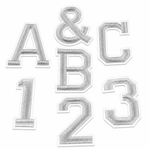 May include: A collection of silver glittery iron-on patches featuring the letters A, B, and C, the numbers 1, 2, and 3, and an ampersand symbol. Each character has a distinct white border and a textured, sparkling finish on a white background.