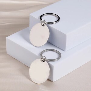 May include: Two silver keychains with round, blank metal tags. The keychains are on a white surface.