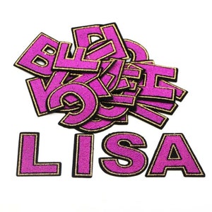 Puede incluir: Letras de fieltro rosa con contorno de purpurina dorada, deletreando el nombre "LISA".
