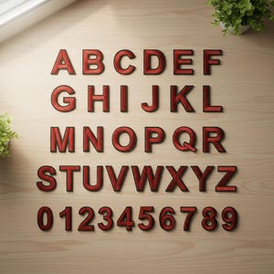 May include: Red wooden alphabet letters and numbers, A through Z and 0 through 9, are arranged on a light wood surface. The letters and numbers have a dark outline and a textured appearance, with a slight shadow effect.