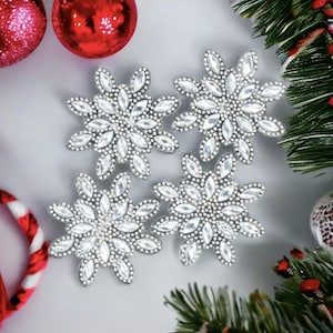Könnte beinhalten: Vier silberne Schneeflocken-Ornamente mit glitzerndem Finish. Jede Schneeflocke besteht aus kleinen, klaren, rautenförmigen Teilen.