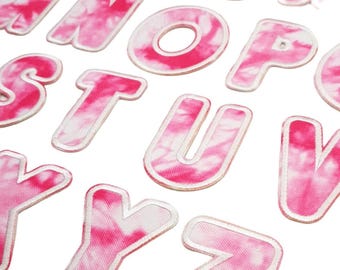 Könnte beinhalten: Eine Sammlung von Stoffbuchstaben mit einem rosa-weißen Batikmuster. Jeder Buchstabe hat einen weißen Rand und ist vor einem weißen Hintergrund angeordnet. Die Buchstaben sind in verschiedenen Schriftarten und Größen erhältlich, ideal für Bastelprojekte.