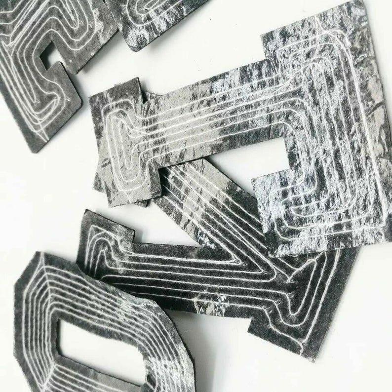 Peut inclure: Un ensemble de cinq lettres en feutre gris avec des coutures blanches, formant le mot "DIY". Les lettres ont un aspect vieilli et vintage.