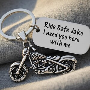 May include: Silver motorcycle keychain with a detailed motorcycle charm and a tag that reads "Ride Safe Jake I need you here with me". The keychain is attached to a silver keyring.