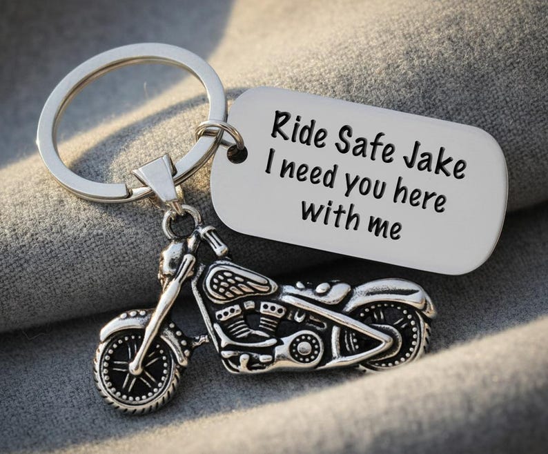 May include: Silver motorcycle keychain with a detailed motorcycle charm and a tag that reads "Ride Safe Jake I need you here with me". The keychain is attached to a silver keyring.