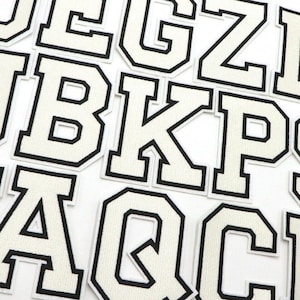 Könnte beinhalten: Weiße Filzbuchstaben mit schwarzen Umrandungen. Die Buchstaben sind in einer großen, fetten Schriftart. Die Buchstaben sind in zufälliger Reihenfolge angeordnet.