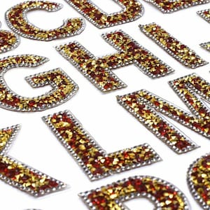 May include: A set of iron-on alphabet letters made of red and gold rhinestones. The letters are arranged in alphabetical order.