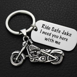 May include: Silver motorcycle keychain with a key ring and a rectangular tag. The tag has the text "Ride Safe Jake I need you here with me". The motorcycle charm is detailed with wheels, engine, and handlebars.