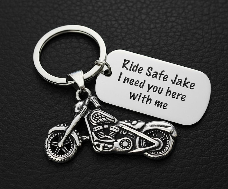 May include: Silver motorcycle keychain with a key ring and a rectangular tag. The tag has the text "Ride Safe Jake I need you here with me". The motorcycle charm is detailed with wheels, engine, and handlebars.