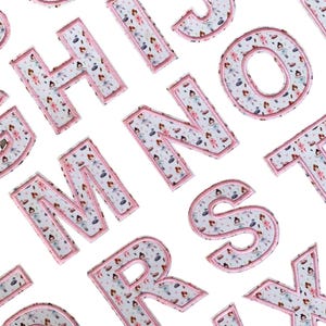 May include: Pink felt letters of the alphabet with a ballerina pattern. Each letter is outlined in white.