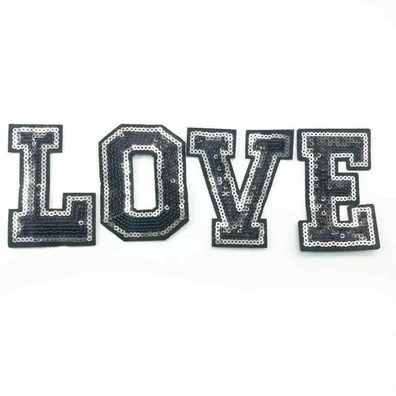 Peut inclure: Patch thermocollant en sequins noirs et argent&eacute;s qui &eacute;pelle le mot "LOVE" en grandes lettres majuscules.