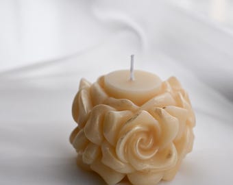 Può includere: Una candela a forma di rosa, con uno stoppino bianco e una cera di colore crema.