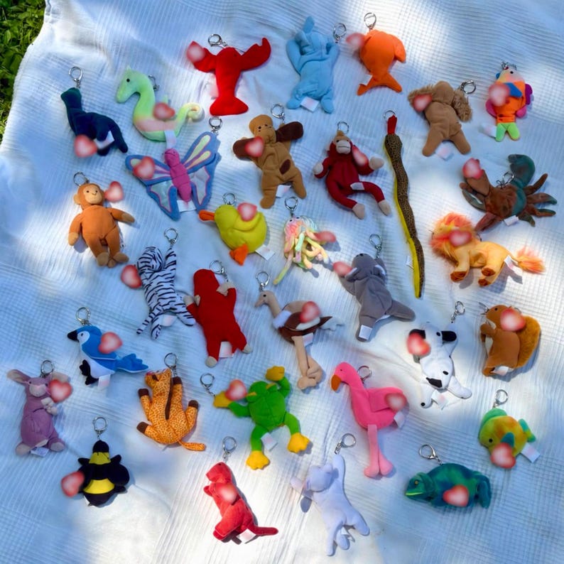 K&ouml;nnte beinhalten: Eine Sammlung verschiedener Pl&uuml;schtier-Schl&uuml;sselanh&auml;nger, darunter ein Hummer, ein Schmetterling, ein Affe, ein Frosch, ein Flamingo, eine Biene und andere Tiere in verschiedenen Farben wie Rot, Blau, Gelb, Gr&uuml;n und Braun, jeweils mit Metallring.