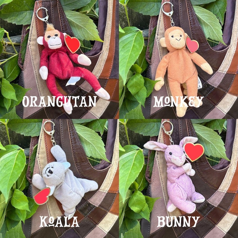 K&ouml;nnte beinhalten: Eine Sammlung von vier Pl&uuml;schtier-Schl&uuml;sselanh&auml;ngern, bestehend aus einem roten Orang-Utan, einem beigen Affen, einem grauen Koala und einem hellvioletten Hasen. Jedes Stofftier hat einen silbernen Metallring und ein rotes herzf&ouml;rmiges Etikett.