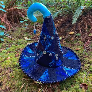 May include: A blue and black witch hat with a pointed crown and a curled brim. The hat is decorated with silver charms, beads, and stitching.