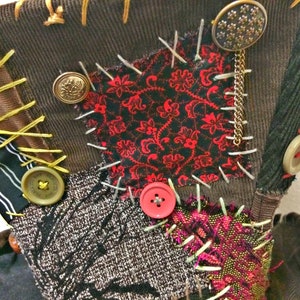 May include: A patchwork textile composed of diverse fabrics like corduroy, patterned red and black fabric, and tweed. It features visible stitching, buttons, and a decorative chain. The color scheme includes brown, red, black, and beige.