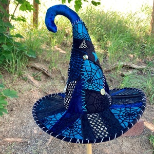 May include: A blue and black witch hat with a pointed crown and a wide brim. The hat is decorated with a spiderweb pattern and various embellishments, including a silver charm.