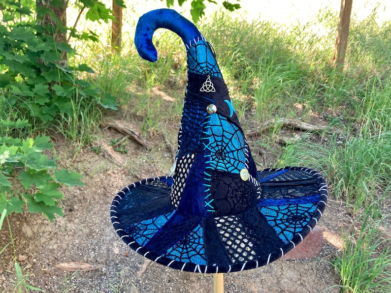 May include: A blue and black witch hat with a pointed crown and a wide brim. The hat is decorated with a spiderweb pattern and various embellishments, including a silver charm.