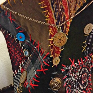 May include: A patchwork hat in brown, green, and red fabrics. It features decorative stitching, buttons, and a pocket watch pendant. The hat's design has a vintage, whimsical aesthetic. The hat is a unique accessory.