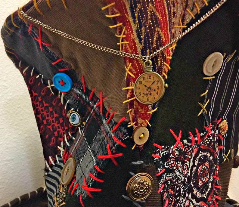 May include: A patchwork hat in brown, green, and red fabrics. It features decorative stitching, buttons, and a pocket watch pendant. The hat's design has a vintage, whimsical aesthetic. The hat is a unique accessory.