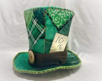 May include: A green top hat with a patchwork design, a brown band, and a wooden button. The hat has a tag that says "10/6".
