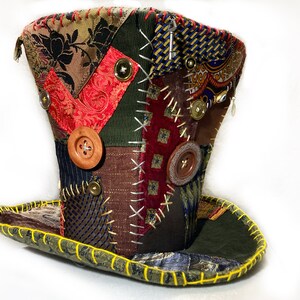 May include: A patchwork top hat with a wide brim, showcasing diverse fabric patterns and colours, such as floral, paisley, and striped designs. The hat is embellished with wooden buttons and decorative stitching, with a yellow stitched brim.
