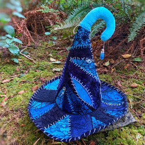 May include: A blue and black witch hat with a pointed crown and a curled brim. The hat is decorated with a spiderweb design and a small blue bottle charm.