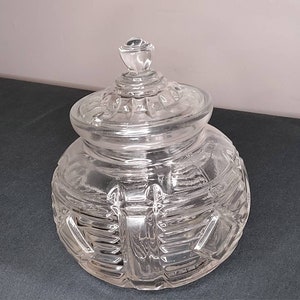 May include: A clear glass jar with a lid. The jar has a geometric pattern and the lid has a knob on top.