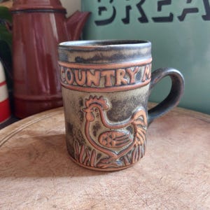May include: A brown ceramic mug with a rooster design and the words "COUNTRY" and "MILL" on the side.