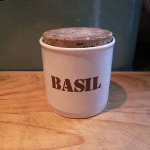 May include: White ceramic jar with a cork lid and the word "BASIL" printed in brown letters.