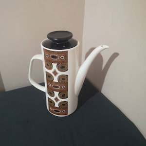 May include: White ceramic coffee pot with a black lid and a brown and white geometric pattern.