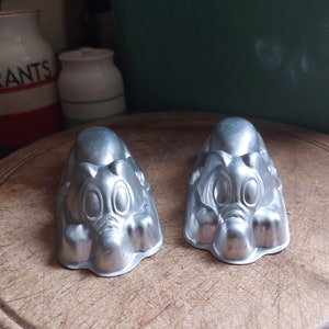 Peut inclure: Deux moules en métal argenté en forme d'éléphants de dessin animé. Les moules sont posés sur une planche à découper en bois.