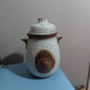 May include: White ceramic jar with a brown lid and a brown design of a peach with the word "Rumtopf" on the front.