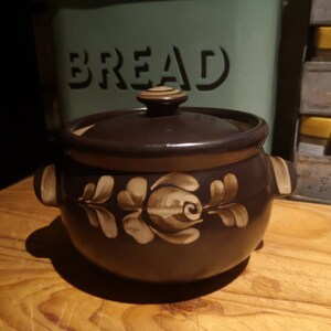 Peut inclure: Un plat en céramique brun avec un couvercle et un motif floral. Le plat a un motif floral blanc avec des accents bruns.