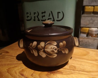 May include: A brown ceramic casserole dish with a lid and a floral design. The dish has a white floral pattern with brown accents.