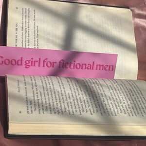 May include: A pink bookmark with the text "Good girl for fictional men" printed in white.