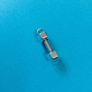 May include: A silver dumbbell charm with a square shape on each end.