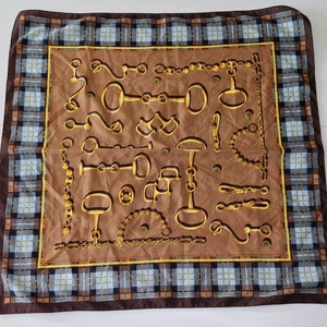May include: A brown silk scarf with a plaid border and a pattern of gold horse bits and chains.