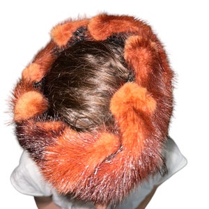 May include: A warm, orange and black fur hat with a unique design. The hat is made of soft, fluffy fur and has a unique, almost abstract pattern.
