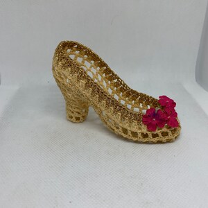 May include: A crocheted shoe with a gold trim and pink flowers. The shoe is made of a light brown material and has a high heel.