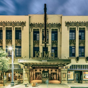 May include: A vintage-style theater building with a sign that reads "KIMO INDIEQ". The building is decorated with intricate details and has a large awning over the entrance.