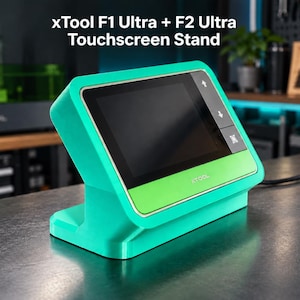 May include: A teal and lime green xTool F1 Ultra + F2 Ultra Touchscreen Stand with a black display screen. The device features a rectangular base, an angled screen housing, and the xTool logo printed on the lower front panel of the unit.